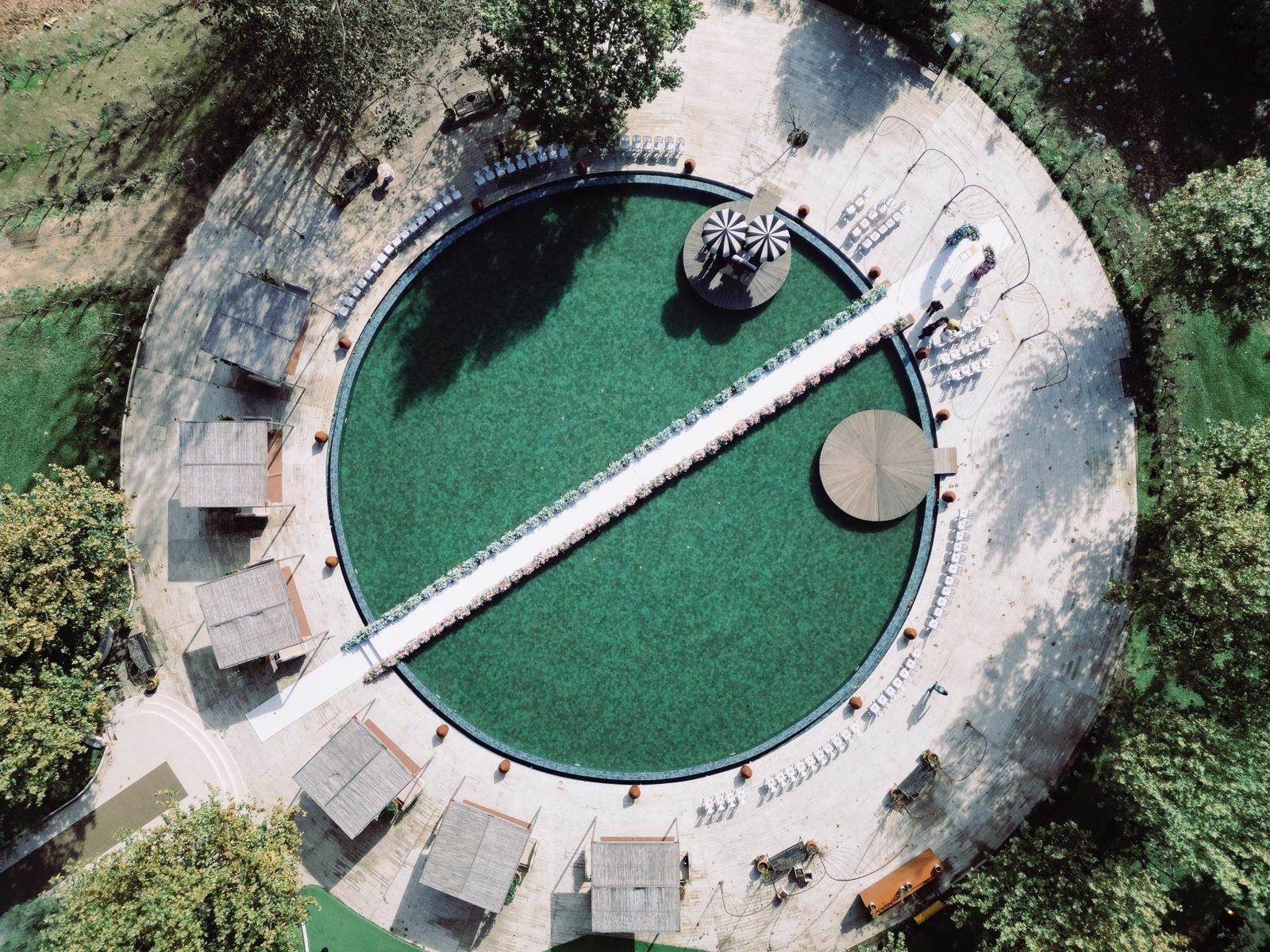 An aerial view of a poolside ceremony with an aisle across the water
